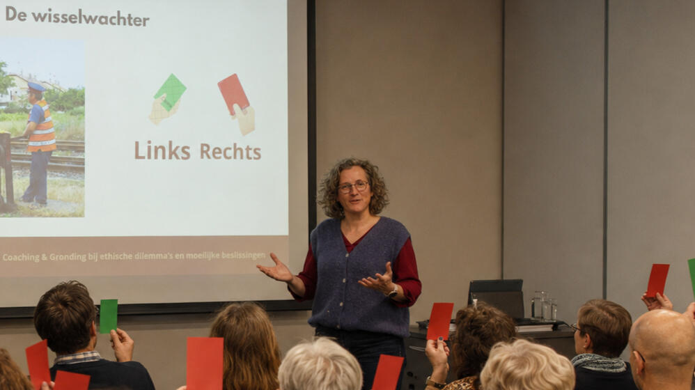 Ils legt een dilemma voor tijdens een training aan een groep mensen, waarbij de deelnemers met rode en groene kaarten een keuze maken
